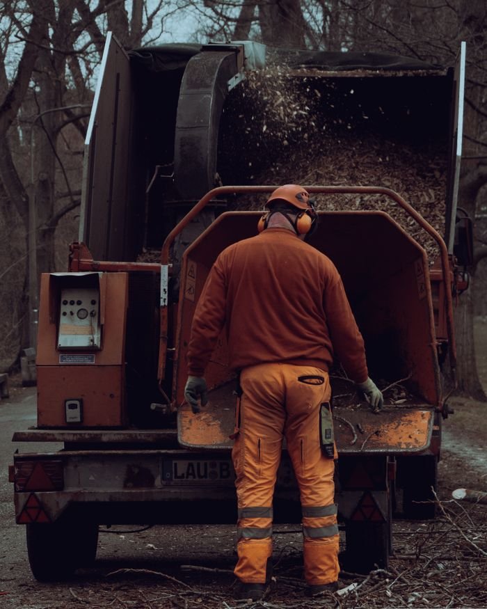 Adult male worker using a wood chipper in an outdoor forest setting.